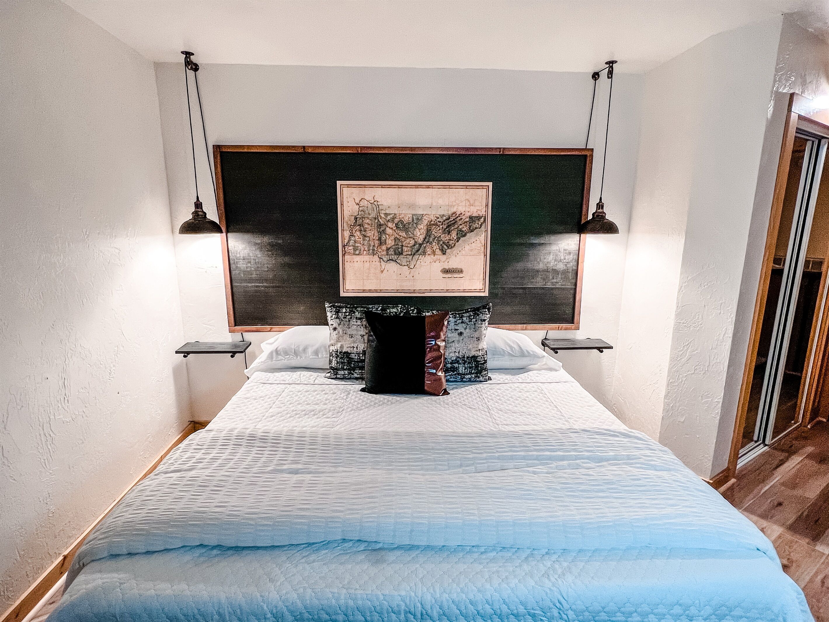 Ein Schlafzimmer mit einem großen Bett, einer Karte an der Kopfteil, zwei Nachttischlampen und einem kleinen Regal.