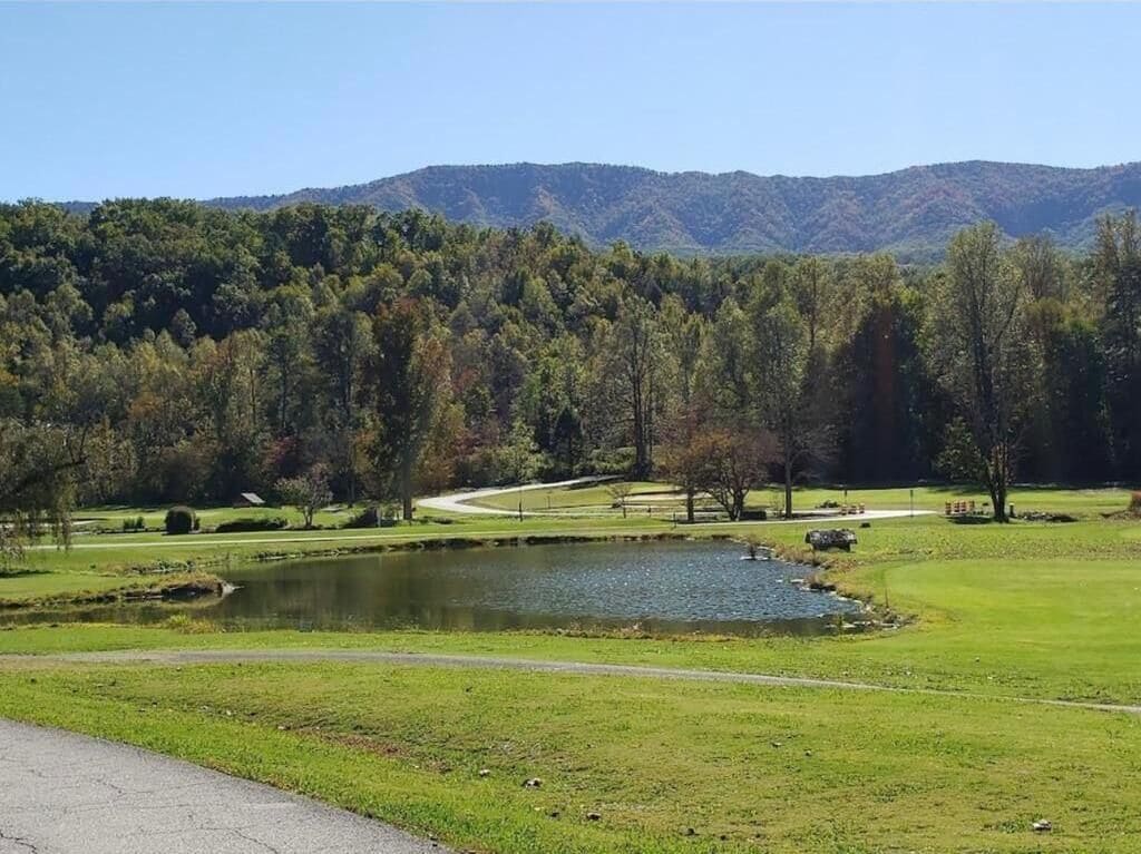 A golf course with a pond, trees, and a mountain in the background.