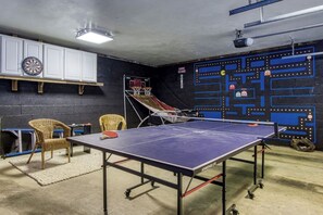 Ein Tischtennisch in einem Raum mit Dartscheibe, Stühlen und einem kleinen Basketballkorb.