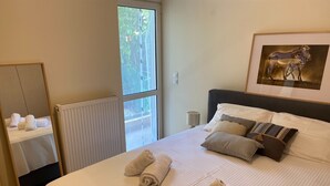 Ein Hotelzimmer mit Bett, Handtüchern, einem Bilderrahmen mit Zebras, einem Heizkörper und einem Fenster mit Blick auf Grünflächen.