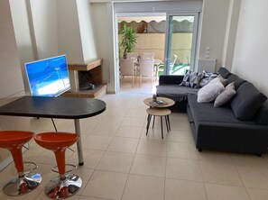 Un salon moderne avec une cheminée, un canapé, un téléviseur et un coin repas équipé de deux tabourets de bar.