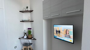 Una camera moderna con una TV a schermo piatto montata a parete, una piccola scrivania con sedia e una mensola con oggetti decorativi.