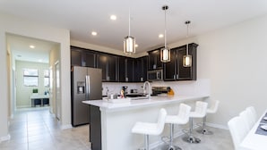 A modern kitchen with dark cabinets, a white island, and bar stools. - Last Minute Disney Getaway! Private Pool & Themed Bedrooms. Book Now! #42647 (Orlando)