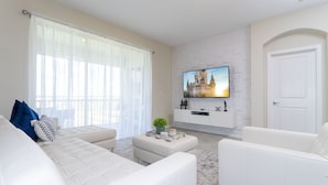 A modern living room with a white sofa set, a flat-screen TV mounted on a white brick wall, and a door to the right. - Last Minute Disney Getaway! Private Pool & Themed Bedrooms. Book Now! #42647 (Orlando)