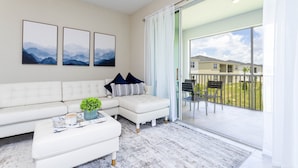 A modern living room with a white sectional sofa, a coffee table with a plant, and a large sliding glass door leading to a balcony. - Last Minute Disney Getaway! Private Pool & Themed Bedrooms. Book Now! #42647 (Orlando)