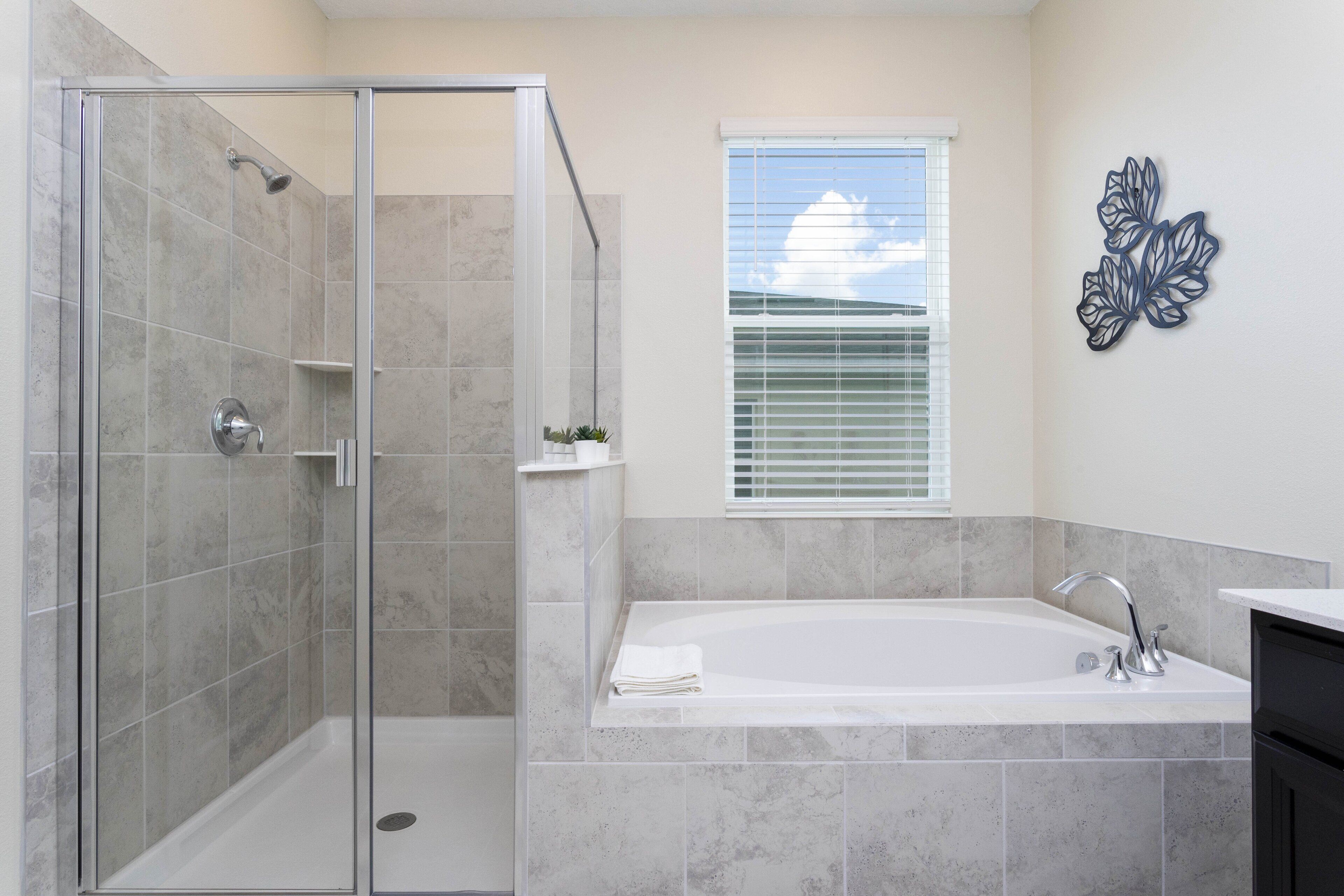 A modern bathroom with a glass-enclosed shower, a freestanding bathtub, and a window with blinds.