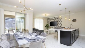 A modern kitchen with a central island, a dining area with a table set for six, and a living area with a sofa and TV. - Last Minute Disney Getaway! Townhouse with Private Pool. Book Now! #38174 (Orlando)