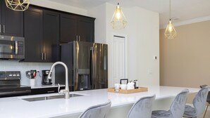 A modern kitchen with dark cabinets, stainless steel appliances, a white countertop, and a bar area with grey chairs. - Last Minute Disney Getaway! Townhouse with Private Pool. Book Now! #38174 (Orlando)