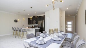 A modern dining area with a long table set for six, surrounded by grey upholstered chairs. - Last Minute Disney Getaway! Townhouse with Private Pool. Book Now! #38174 (Orlando)