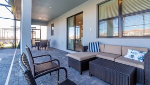 Ein Terrassenbereich im Freien mit Korbmöbeln, einer gepolsterten Couch und einer Glastür zu einem Innenraum.