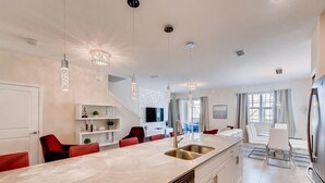 Een moderne keuken met een centraal kookeiland, roestvrijstalen apparatuur en hangende lampen.