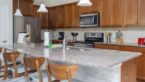 Eine Küche mit Granit Arbeitsplatten, Holzschränken, Edelstahlgeräten und Pendelleuchten.