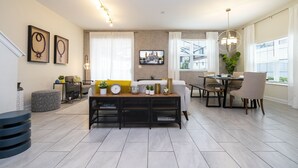 A modern living room with a dining area, featuring a sofa, a coffee table, and a dining table with chairs. There are decorative items on the coffee table and a plant on the dining table.