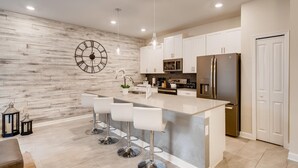 A modern kitchen with a central island, white cabinetry, stainless steel appliances, and a large wall clock. - Last Minute Disney Getaway! Townhouse with Private Pool. Book Now! #43297 (Orlando)