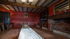 Une salle à manger avec une longue table en bois, des chaises, un tapis et une cheminée en briques.