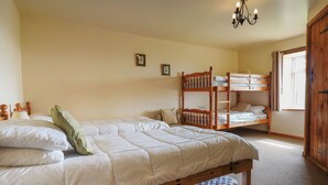 Une chambre avec un grand lit, un lit superposé, une armoire en bois et un lustre.