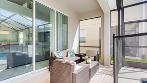A modern balcony with wicker furniture, a glass door leading to a pool, and a view of the surrounding area. - Last Minute Disney Getaway! Luxury Villa with Private Pool & Game Room. Book Now! #43331 (Orlando)