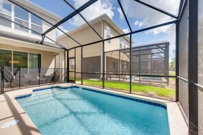 A swimming pool with a glass enclosure, a covered patio area, and a view of a house in the background.