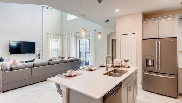 A modern kitchen with a central island, stainless steel appliances, and a grey sofa in the living area. - Last Minute Disney Getaway! Luxury Villa with Private Pool & Game Room. Book Now! #43331 (Orlando)
