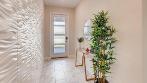 A hallway with a textured wall, a frosted glass door, a mirror, a potted plant, and a glass table with chairs. - Last Minute Disney Getaway! Luxury Villa with Private Pool & Game Room. Book Now! #43331 (Orlando)