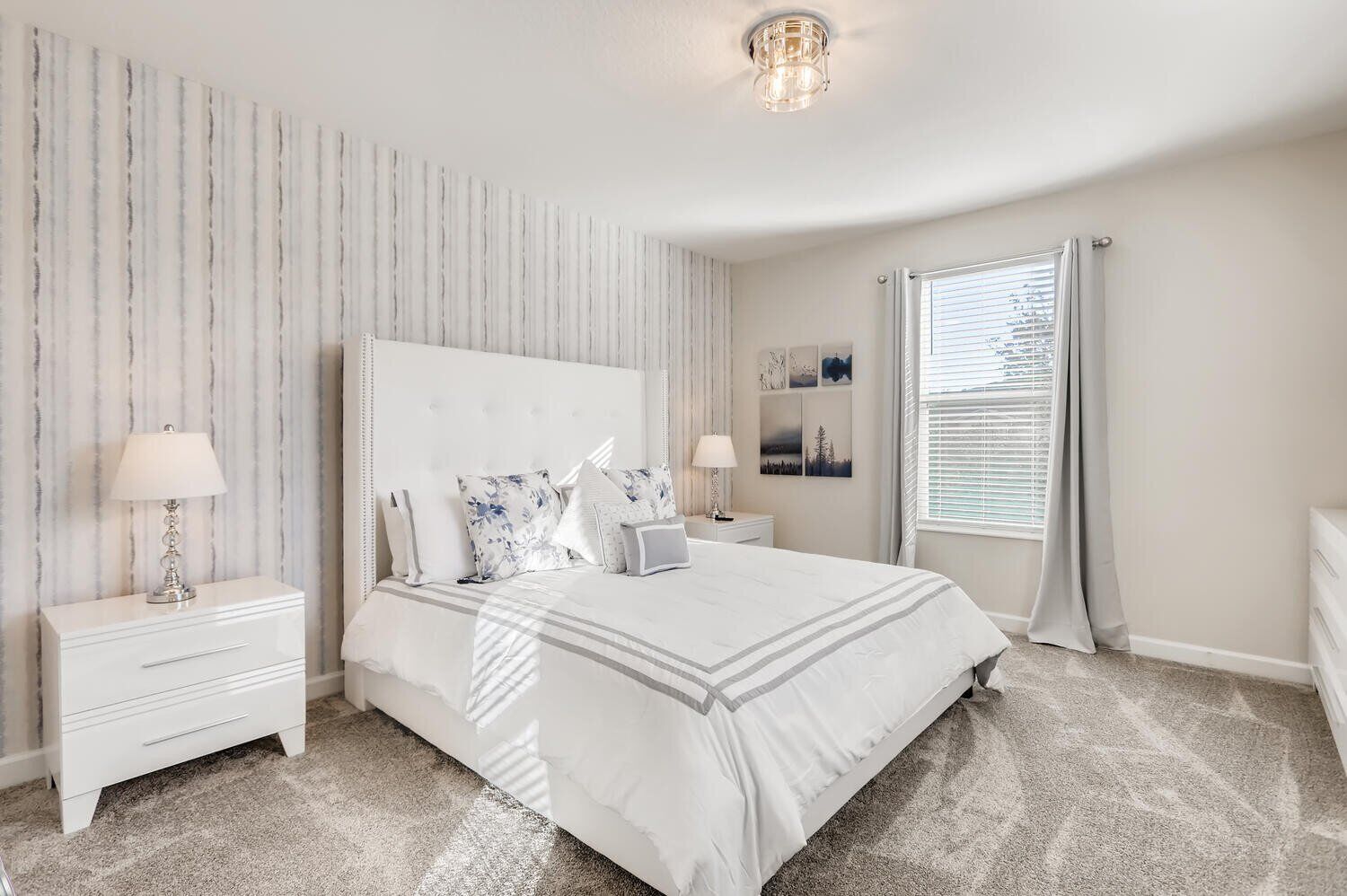 A bedroom with a large bed, two bedside tables, a nightstand, a window with curtains, and a wall with a striped pattern.