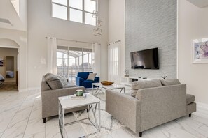 A modern living room with a large TV, two sofas, a coffee table, and a glass partition. - Last Minute Disney! Private Pool, Hot Tub & Themed Bedrooms. Book Now! #43337 (Orlando)