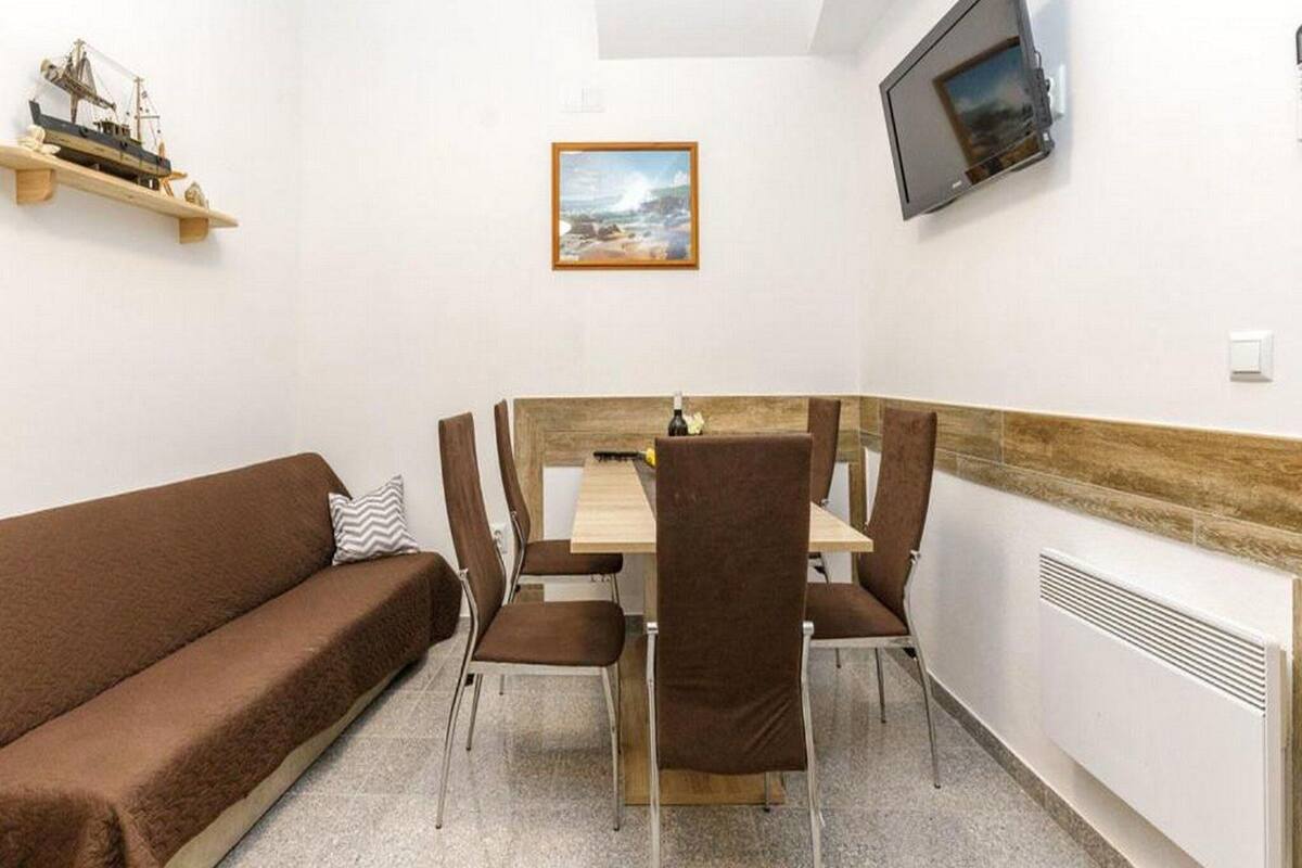 A cozy room with a brown sofa, a wooden table with chairs, a framed picture on the wall, and a TV mounted above the table.