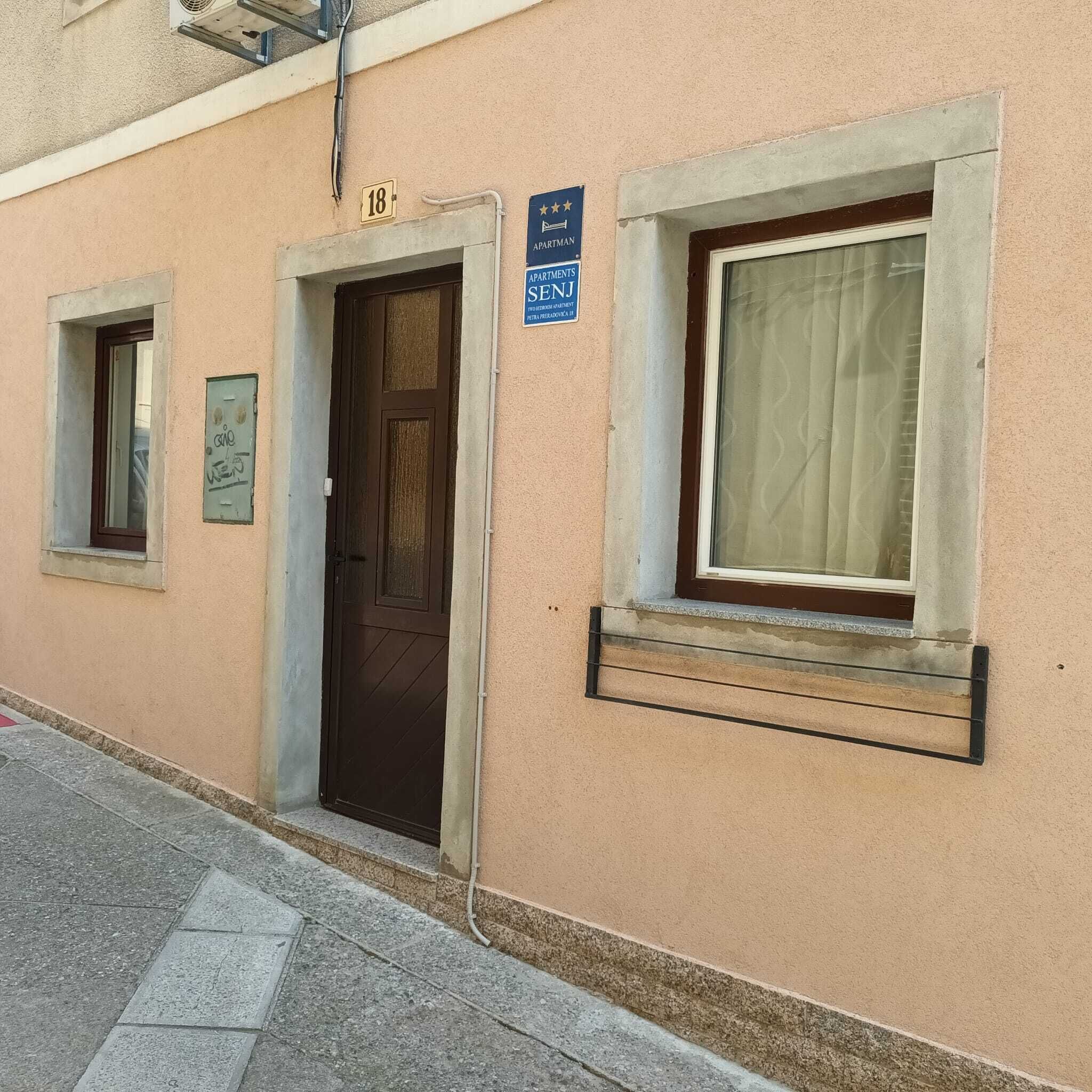 A building with a brown door, a window with a curtain, and a sign indicating it is an apartment building.