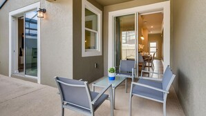 Un patio con dos sillas y una mesa, una puerta corrediza de vidrio y una lámpara fijada a la pared.