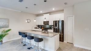 Una cocina moderna con una isla central, taburetes de bar, electrodomésticos de acero inoxidable e iluminación colgante.