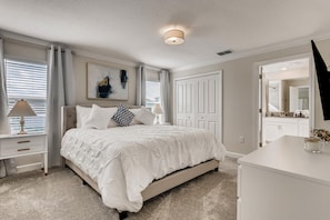 A bedroom with a large bed, a nightstand with a lamp, a dresser, and a painting on the wall.