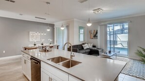 Una cocina moderna con una isla grande, luces colgantes y un rincón comedor con un sofá gris.