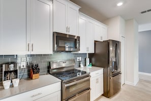 A modern kitchen with stainless steel appliances, white cabinetry, and a tiled backsplash.