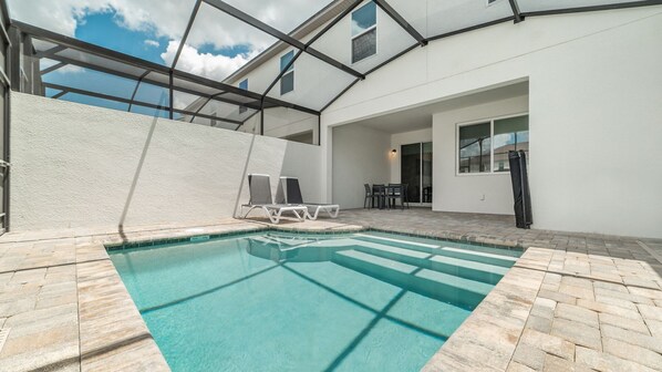A swimming pool with a clear blue water, surrounded by a patio area with lounge chairs and a table.