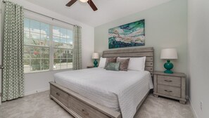 A bedroom with a large bed, two nightstands, a ceiling fan, and a window with curtains.