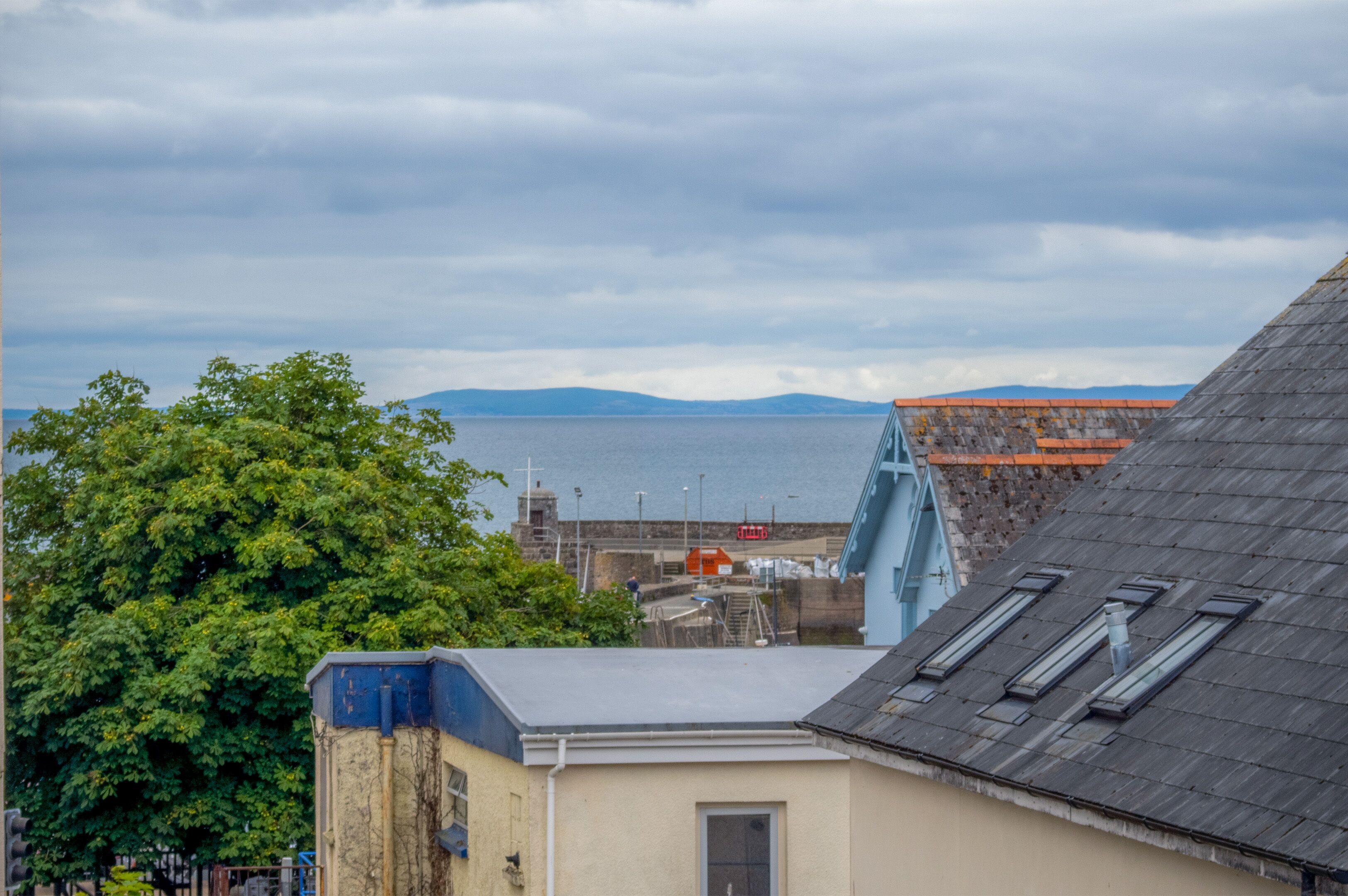 A coastal view with a bridge, a building with a sloped roof, and a tree.