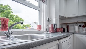 Una cocina moderna con armarios blancos, encimera de granito, pileta de acero inoxidable y una ventana con vistas a casas y árboles.