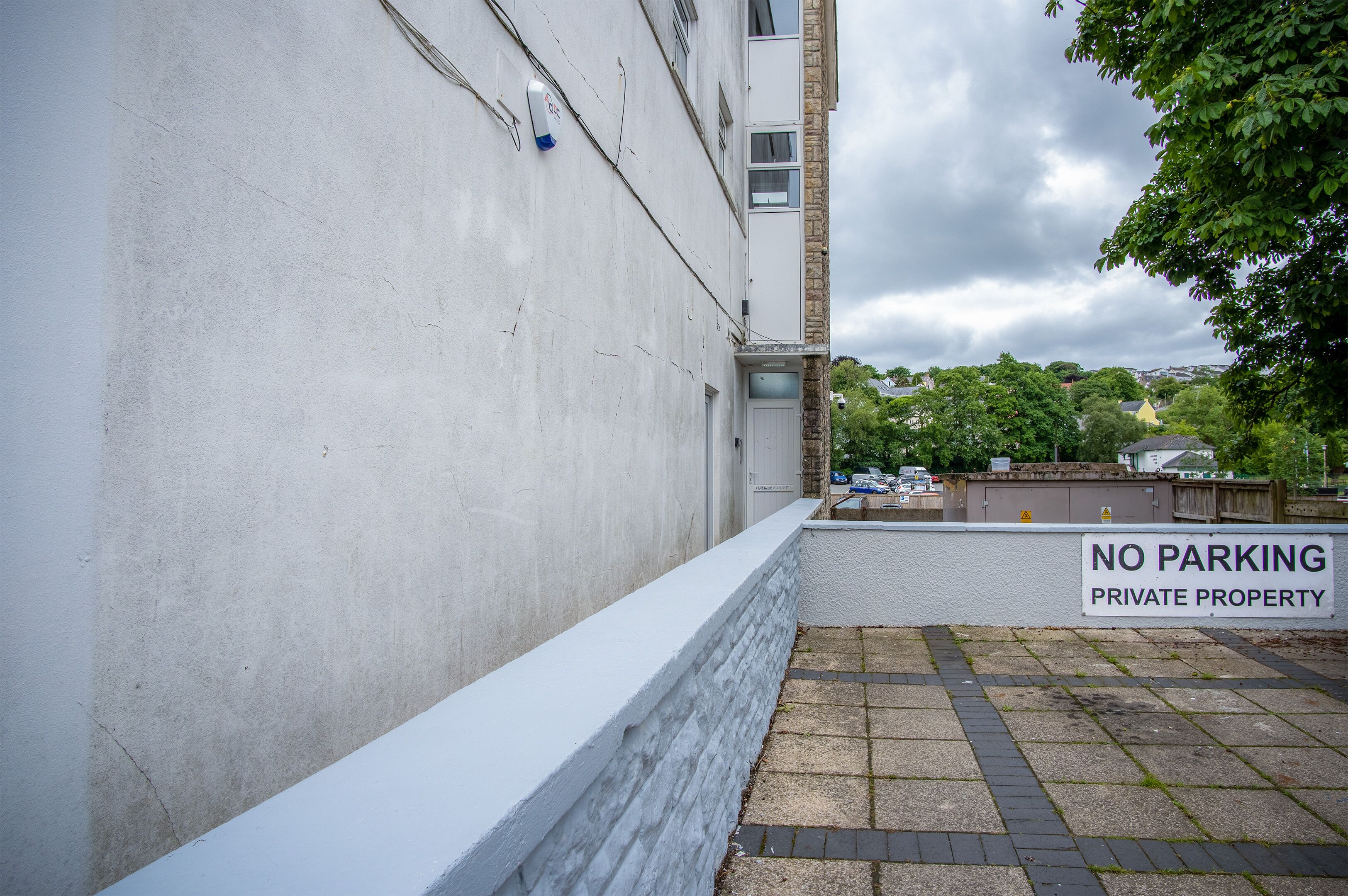 A narrow alleyway with a 'NO PARKING PRIVATE PROPERTY' sign, a white wall, and a paved path.