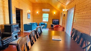 Ein Holzblockhaus-Interieur mit Esstisch, Stühlen, einer Couch, einem Fernseher und einem Kamin.