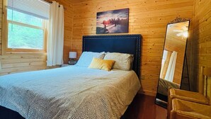 Ein Schlafzimmer einer Holzhütte mit einem Bett, einem Deckenventilator, einem Gemälde und einem Stuhl.