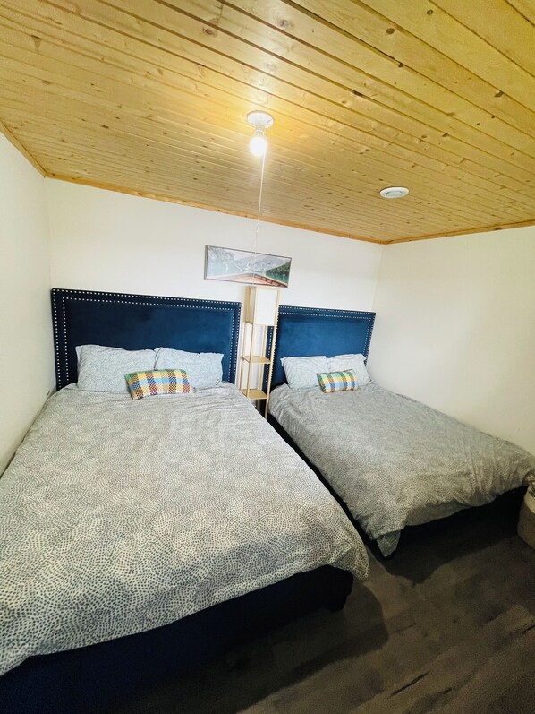 A room with two beds, wooden ceiling, and a painting on the wall. - Chalet Drive - Lakefront Cottage (Windsor)