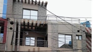 Un edificio de dos plantas con entrada protegida por un portón, un balcón y un pequeño jardín.