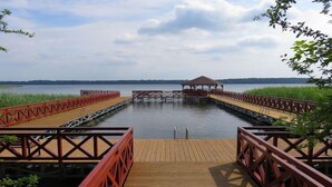 Un muelle de madera que conduce a un área techada con vista a un lago tranquilo y árboles distantes.
