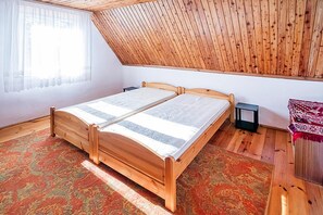 Une chambre avec un lit en bois, un tapis à motifs, une table de chevet et une fenêtre ornée de rideaux légers.
