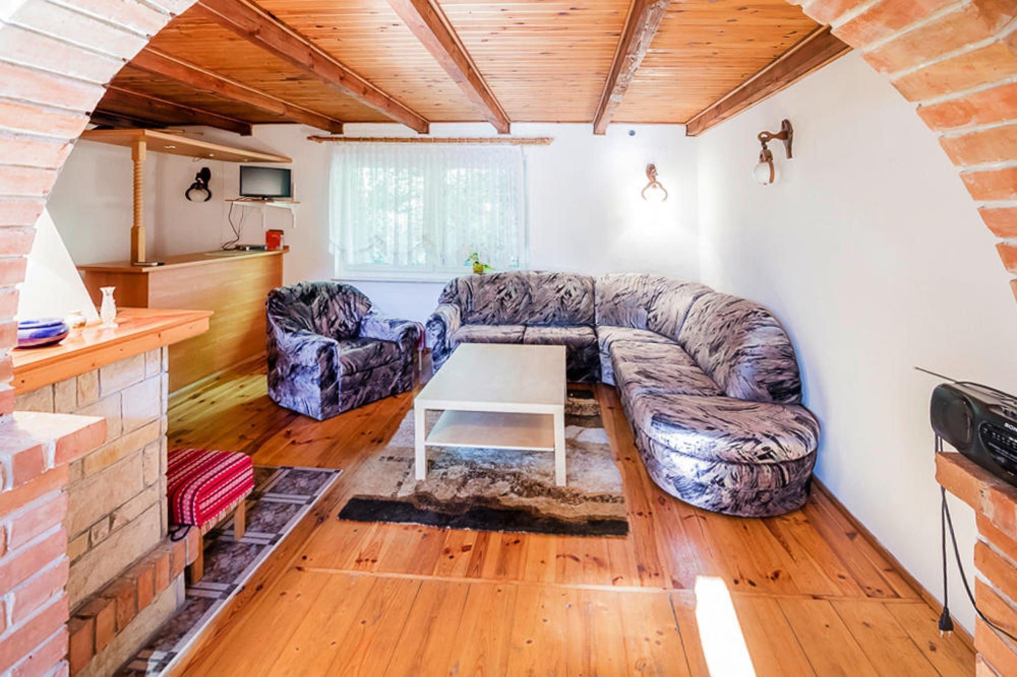 A cozy living room with a wooden ceiling, a brick fireplace, a sofa, a coffee table, and a television.