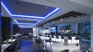 Un restaurant moderne doté d’un bar, de hauts plafonds éclairés de lumière bleue et offrant une vue sur des palmiers.