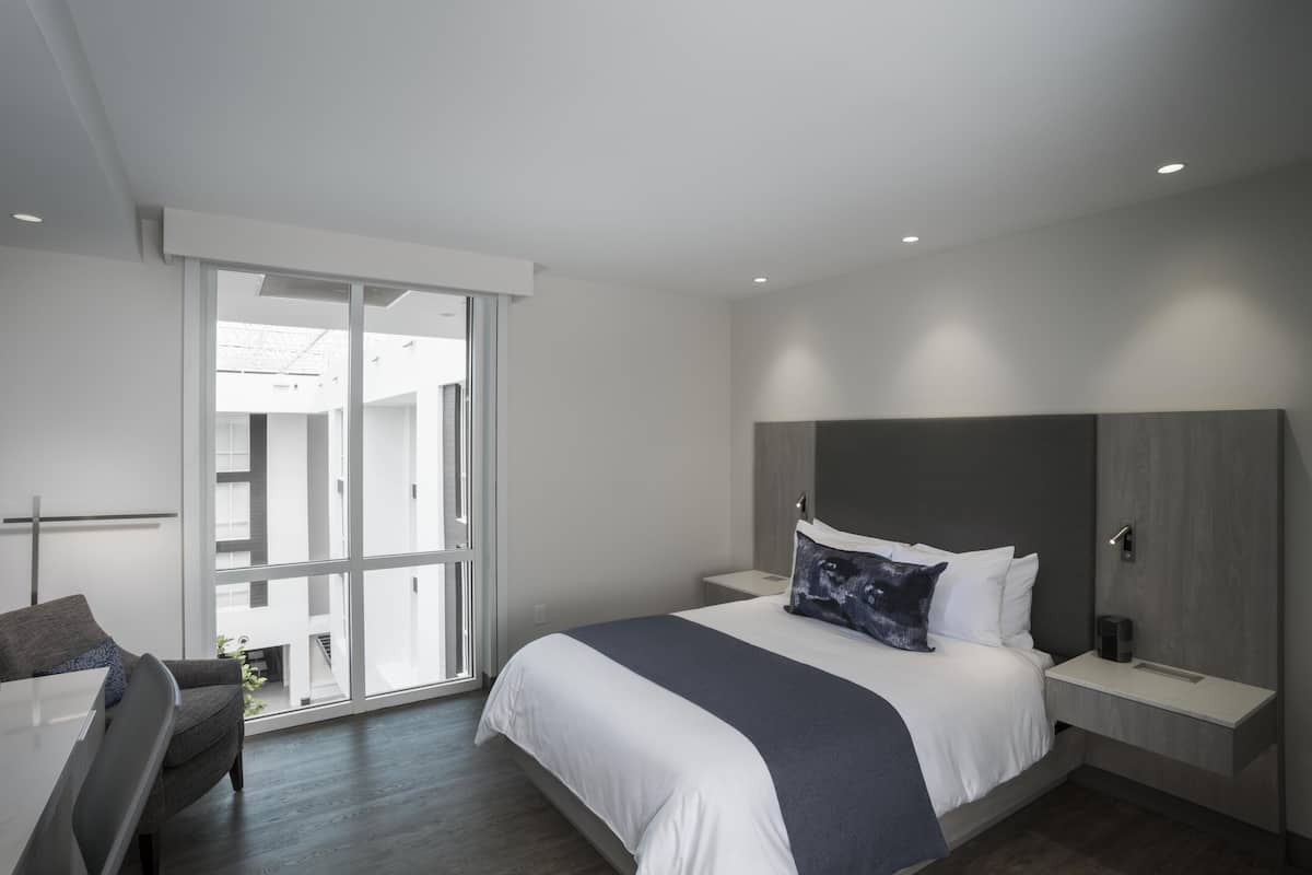 A modern bedroom with a large bed, bedside tables, a desk, and a sliding glass door leading to an outdoor area.