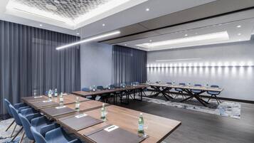 Un salón de conferencias con largas mesas, sillas azules y botellas de agua.