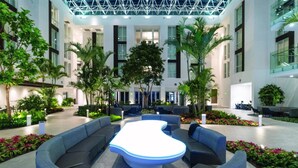 Un hall d’entrée moderne et intérieur, doté d’un espace salon central, entouré de verdure et agrémenté d’un haut plafond avec des poutres apparentes.