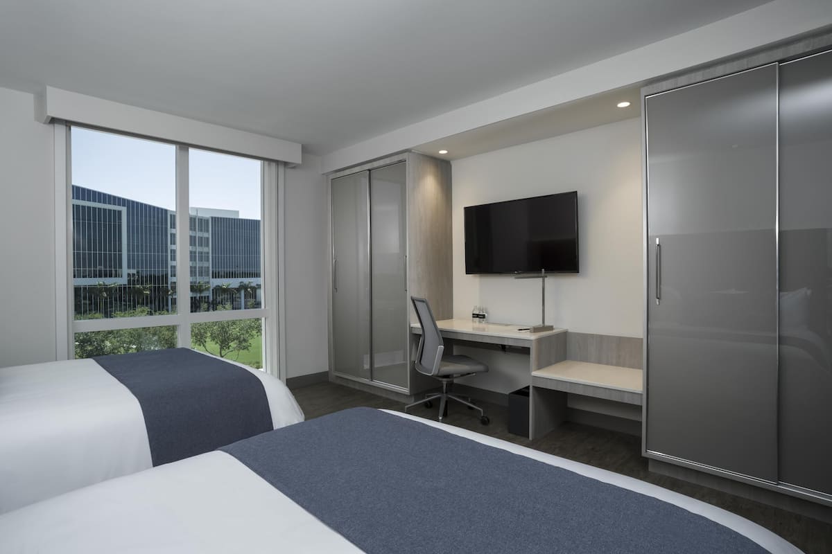 A modern hotel room with two beds, a desk, a chair, a TV, and a wardrobe.